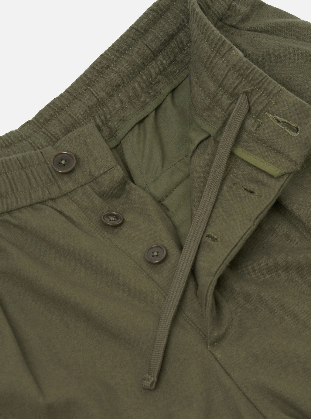 Close-up of olive green drawstring Universal Works trousers  showing the waistband, drawstring, and buttoned placket.