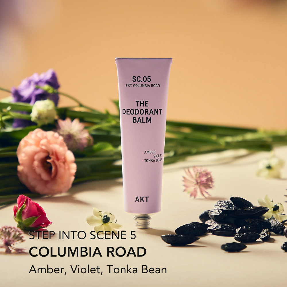 Deodorant balm tube labeled 'SC.05' with flowers and black stones on a wooden surface.
