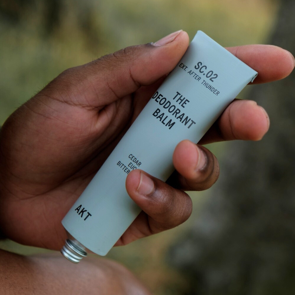 Hand holding a deodorant balm tube labeled 'The Deodorant Balm' by AKT.