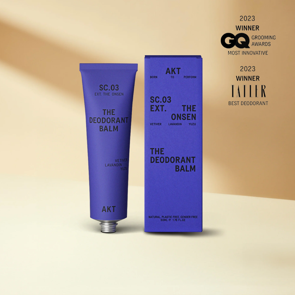 Deodorant balm with blue packaging and 'AKT' branding on a beige background, featuring awards text.