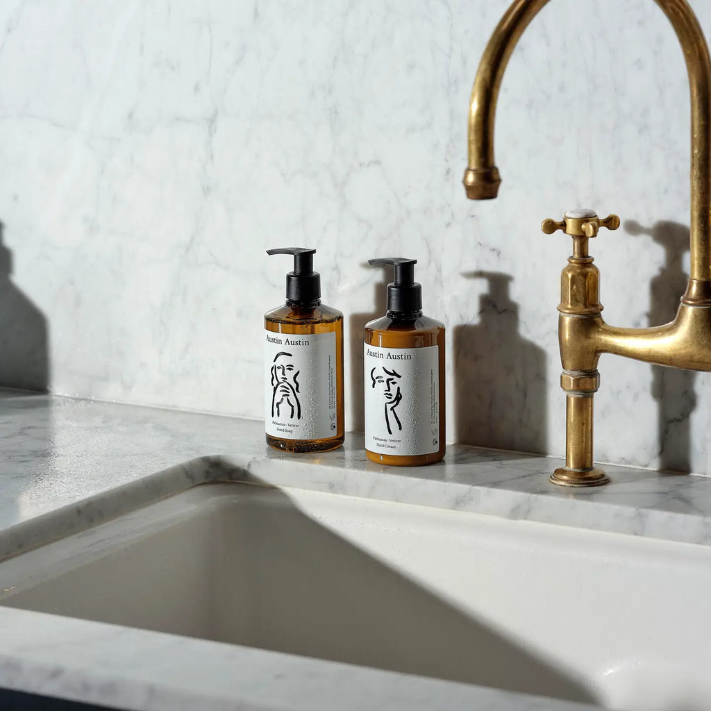 Two bottles of soap on a marble countertop with a brass faucet.