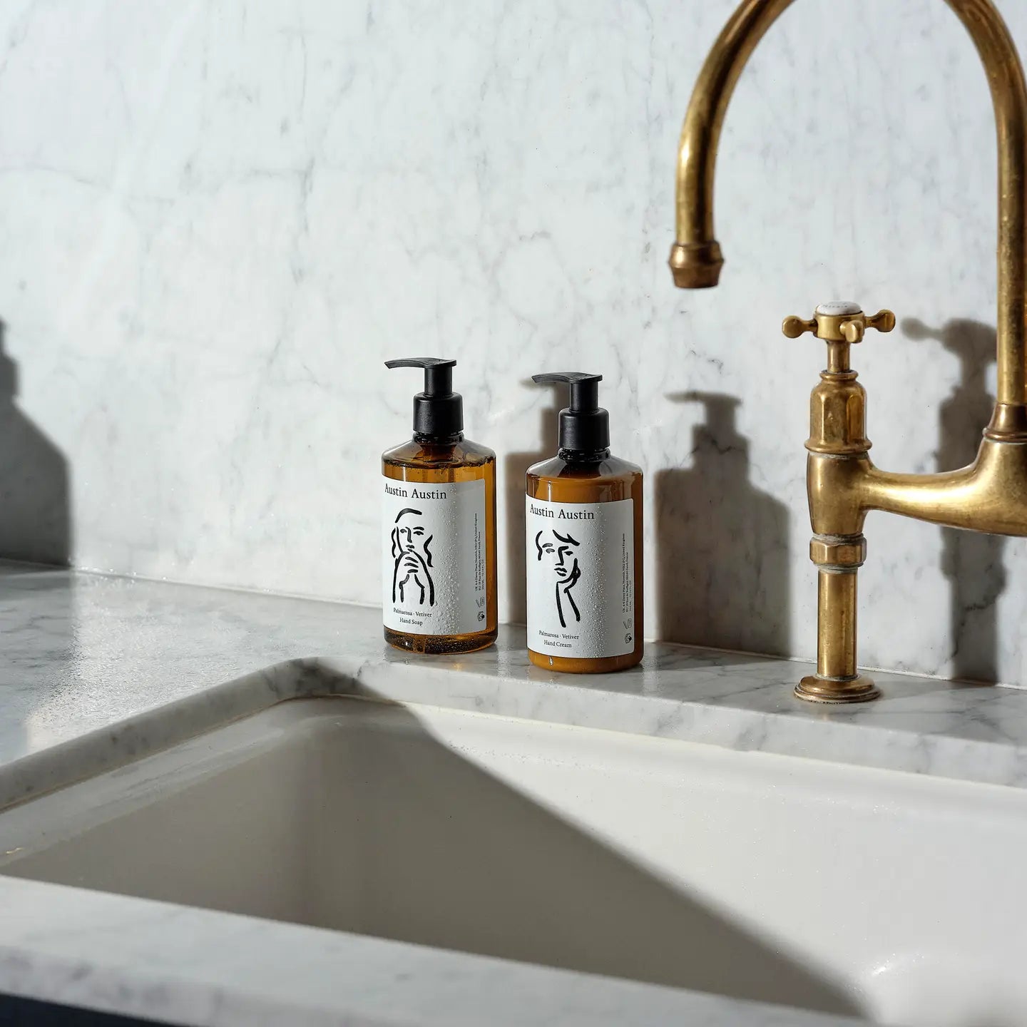 Two bottles of soap on a marble countertop with a brass faucet.