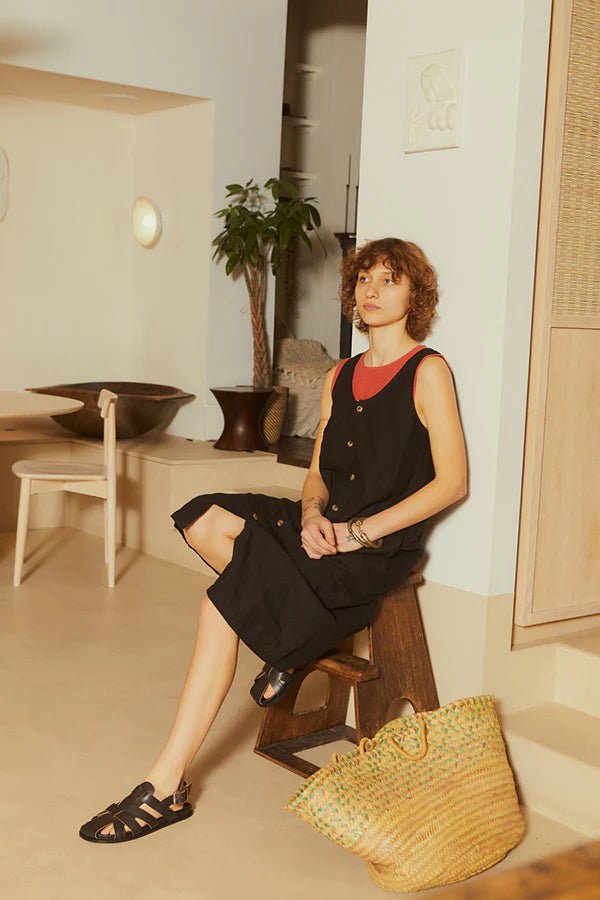 Black sleeveless LF Markey dress with button details with a red sleeveless top underneath photographed on a women sat down in a natural coloured home 