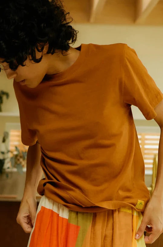 Person wearing a TERRACOTTA LF Markey T-Shirt with a  multicolored skirt in a room.