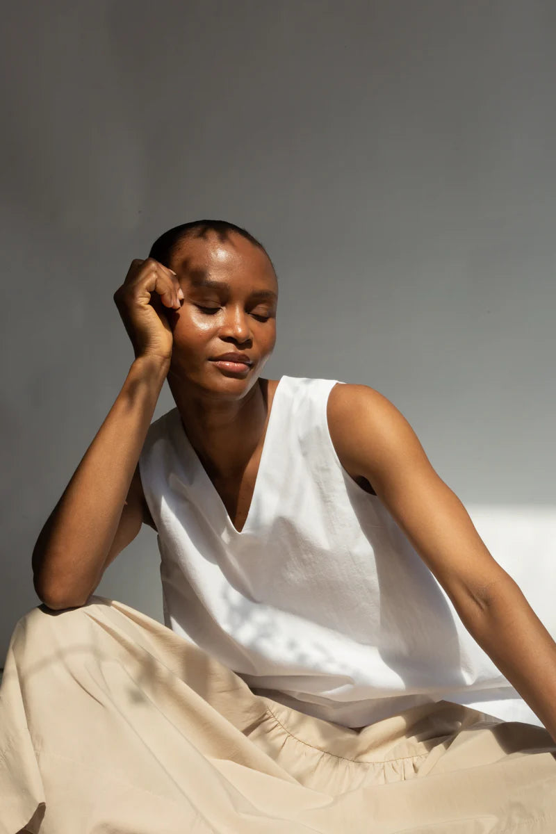 Person wearing a white sleeveless top and beige skirt against a neutral background