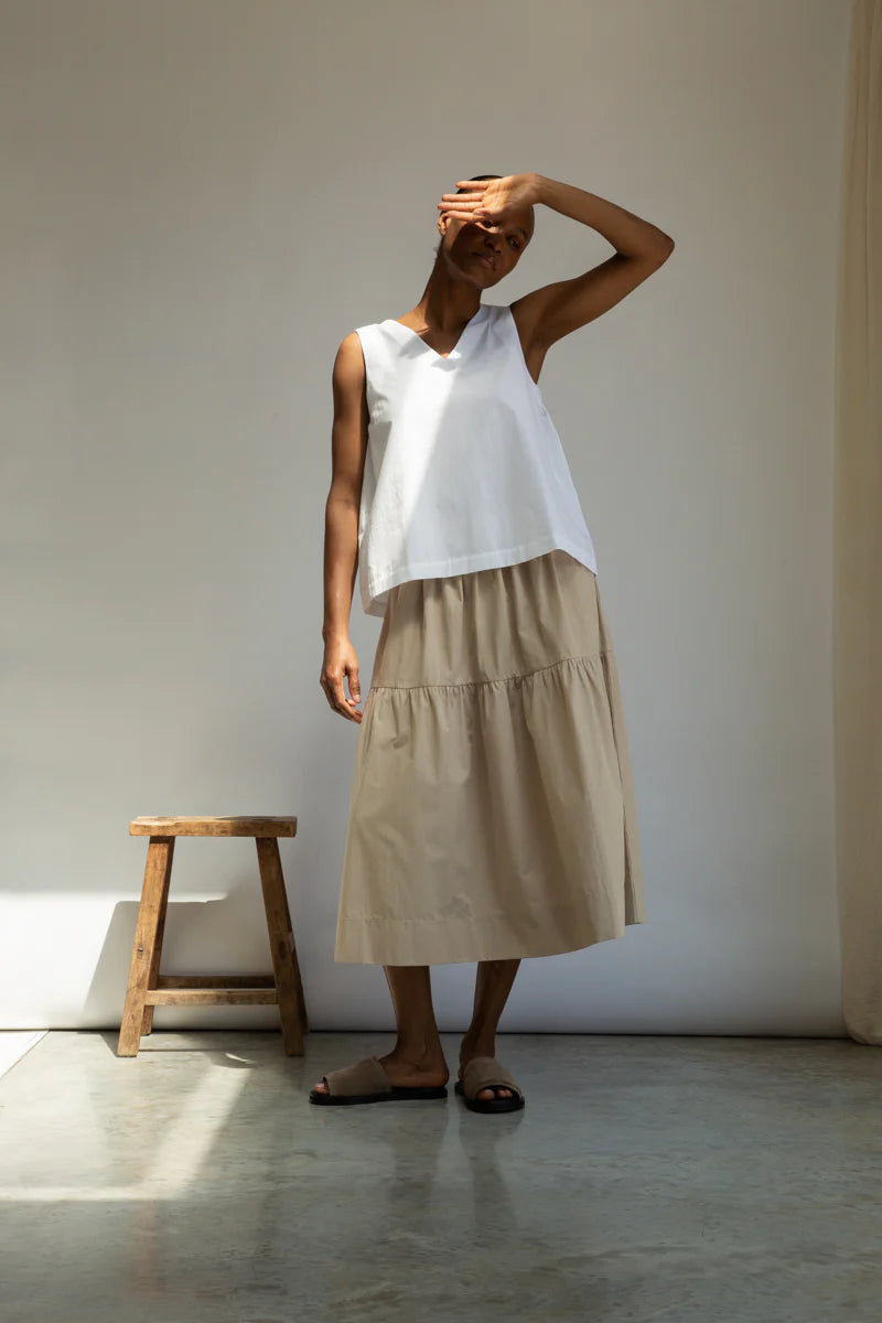 Person wearing a white sleeveless top and beige skirt against a neutral background