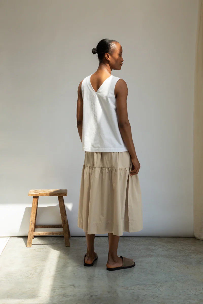Person wearing a white sleeveless top and beige skirt against a neutral background
