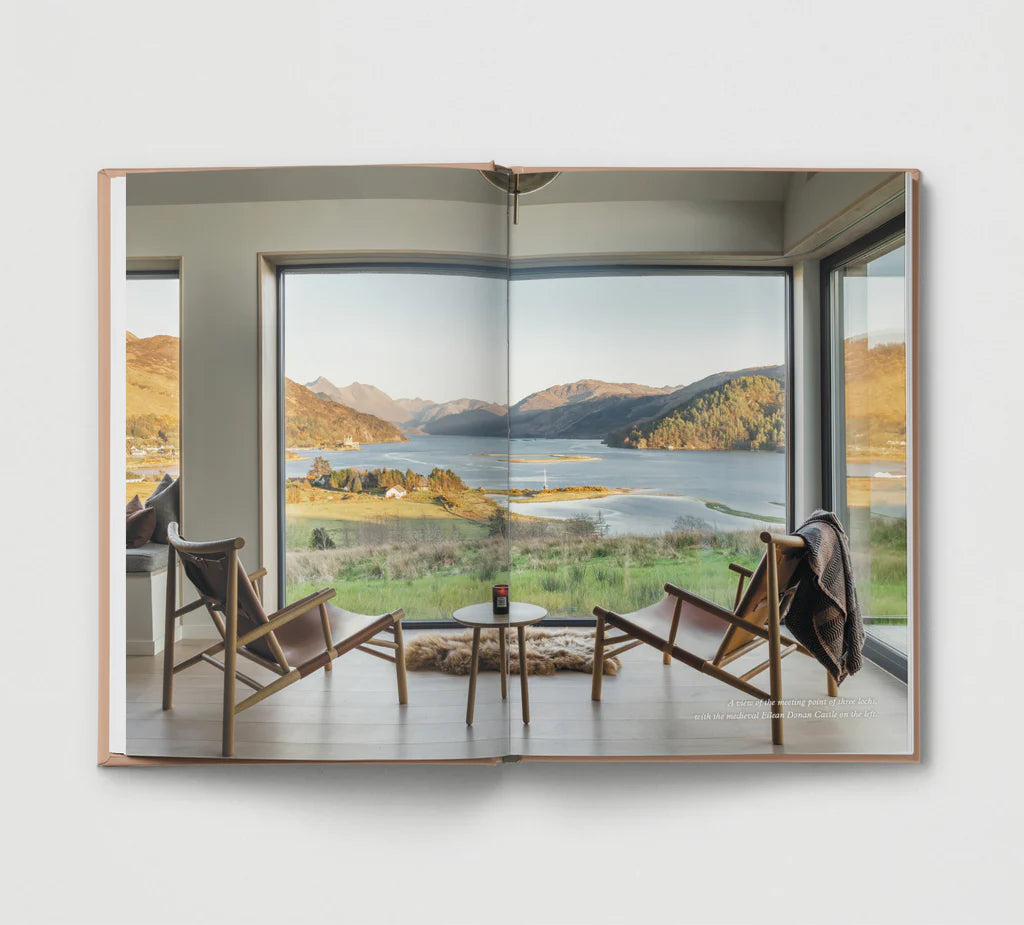 Modern interior with chairs and a table in front of large windows showing a scenic view of mountains and water.