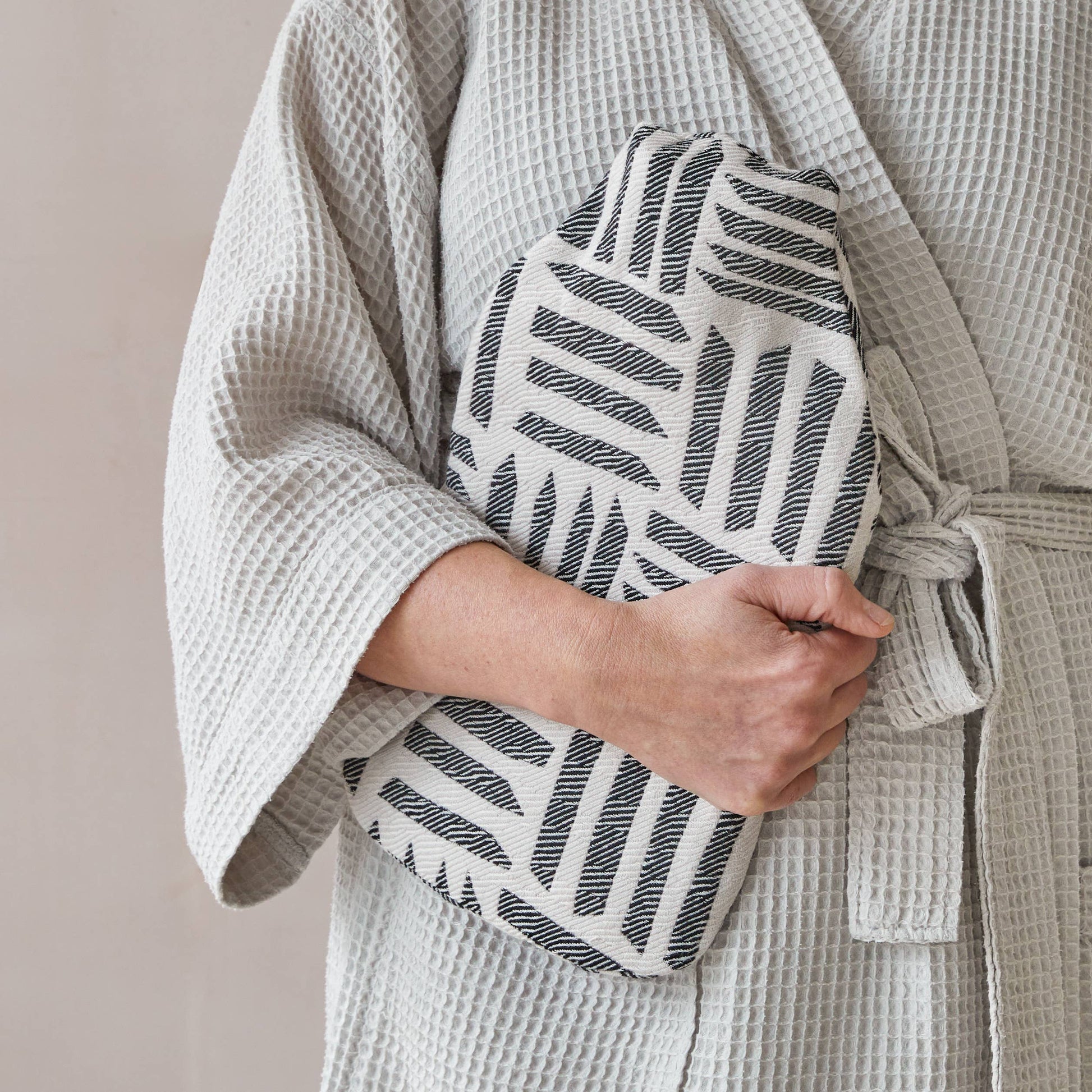 Person wearing a textured robe holding a patterned hot water bottle against a neutral background