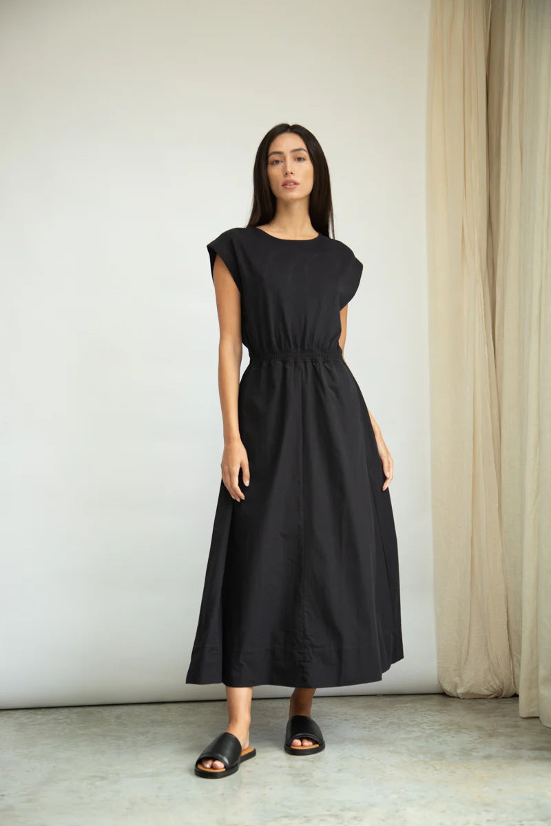 Woman wearing a black dress standing against a plain background