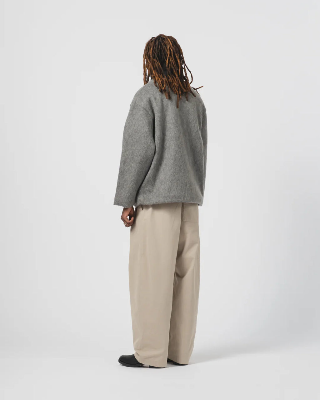 Person wearing anEat Dust grey cardigan and beige trousers on a white background