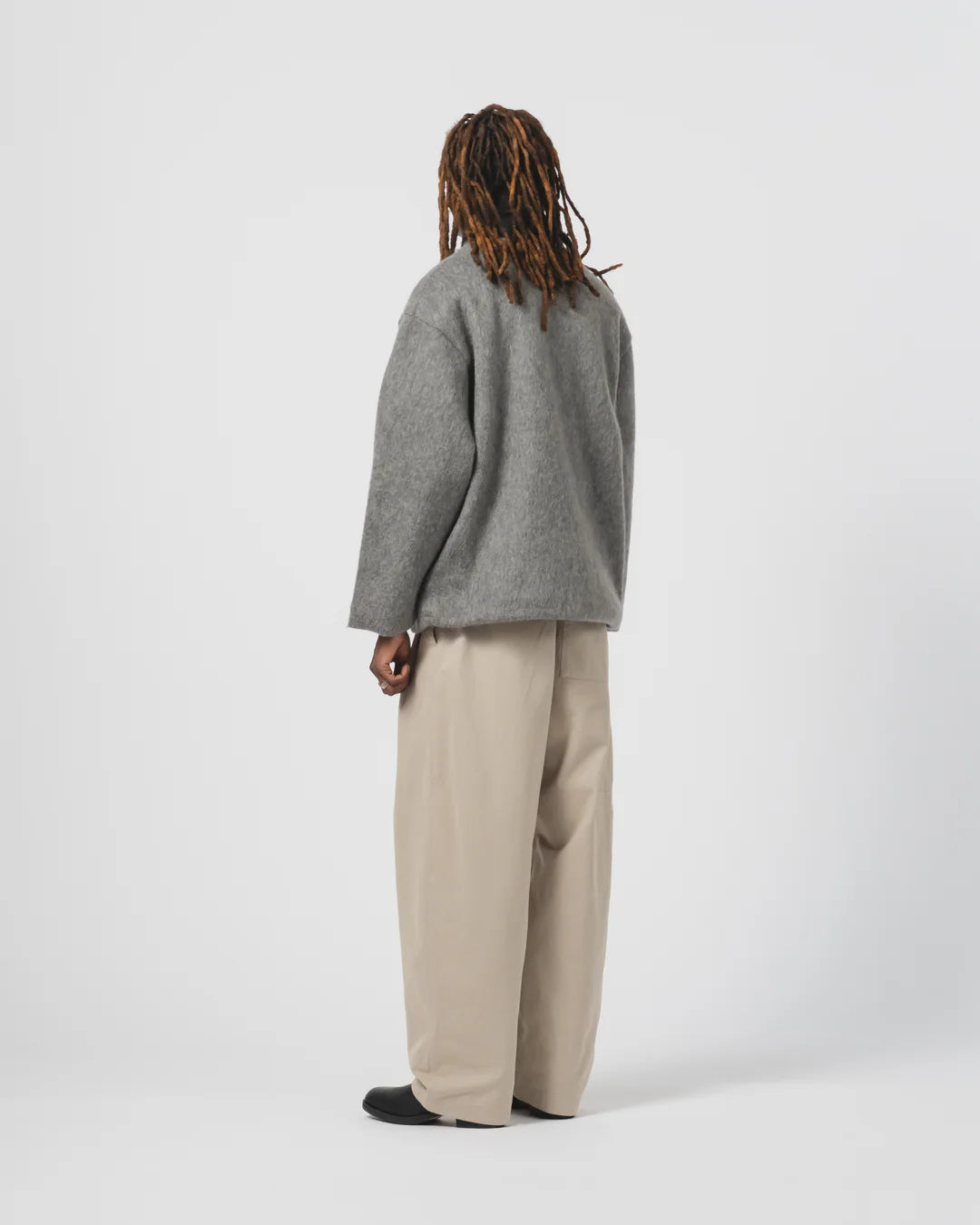 Person wearing anEat Dust grey cardigan and beige trousers on a white background
