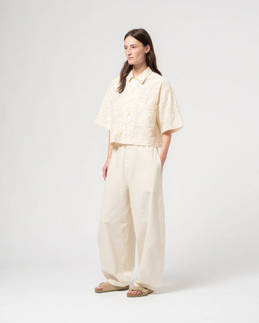 Person wearing a light-colored GIRLS OF DUST shirt and wide-leg pants on a white background