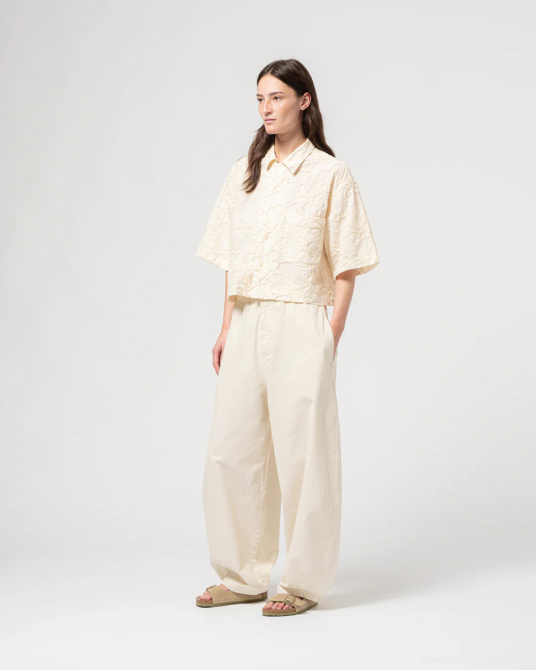 Person wearing a light-colored GIRLS OF DUST shirt and wide-leg pants on a white background