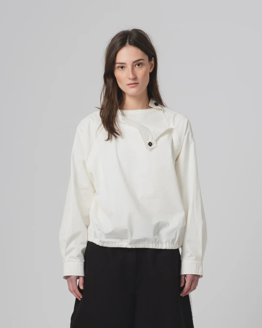 Woman wearing a white Girls of Dust shirt  with black buttons on a plain background