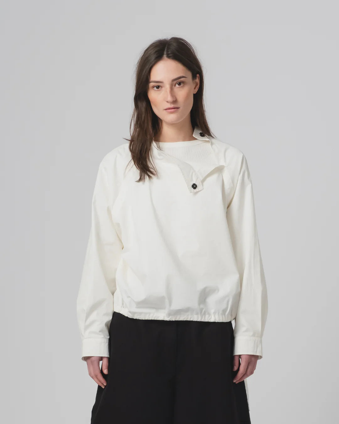 Woman wearing a white Girls of Dust shirt  with black buttons on a plain background