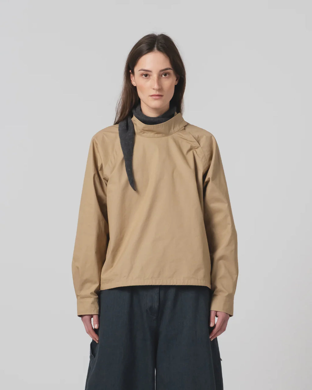 Person wearing a Girls of Dust beige shirt with a black scarf on a plain background