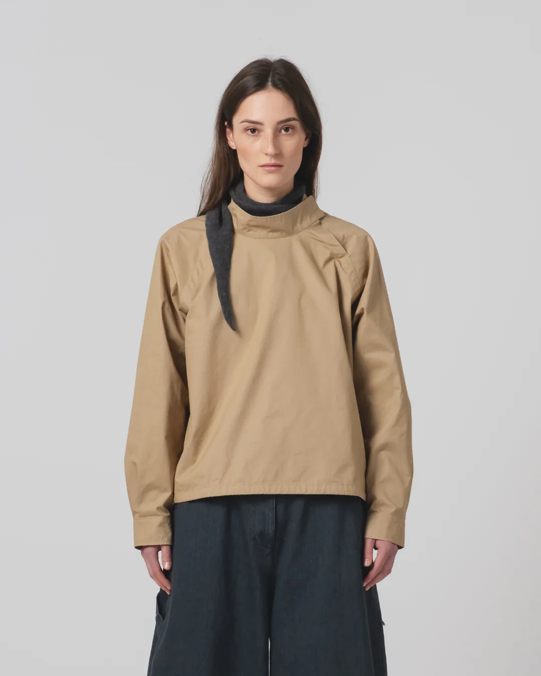 Person wearing a Girls of Dust beige shirt with a black scarf on a plain background