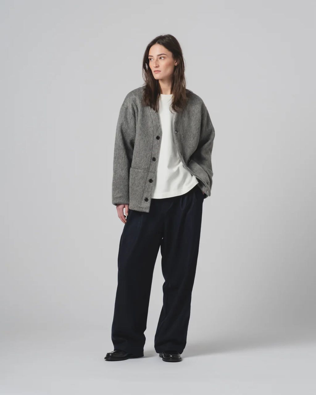 Person wearing a grey cardigan, white shirt, and black pants on a light gray background