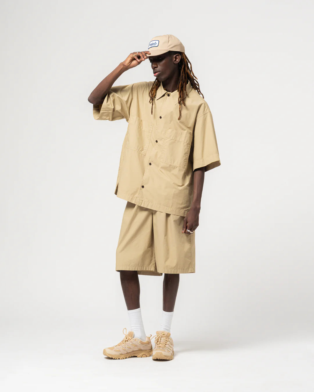 Person wearing beige Eat Dust shirt and shorts against a light grey background 