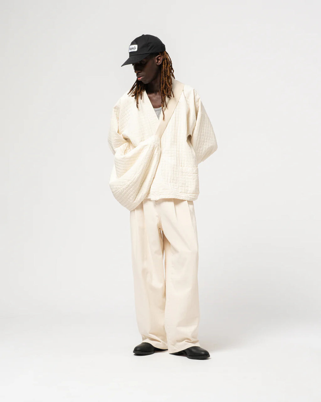 Person wearing a white outfit with a black cap on a white background