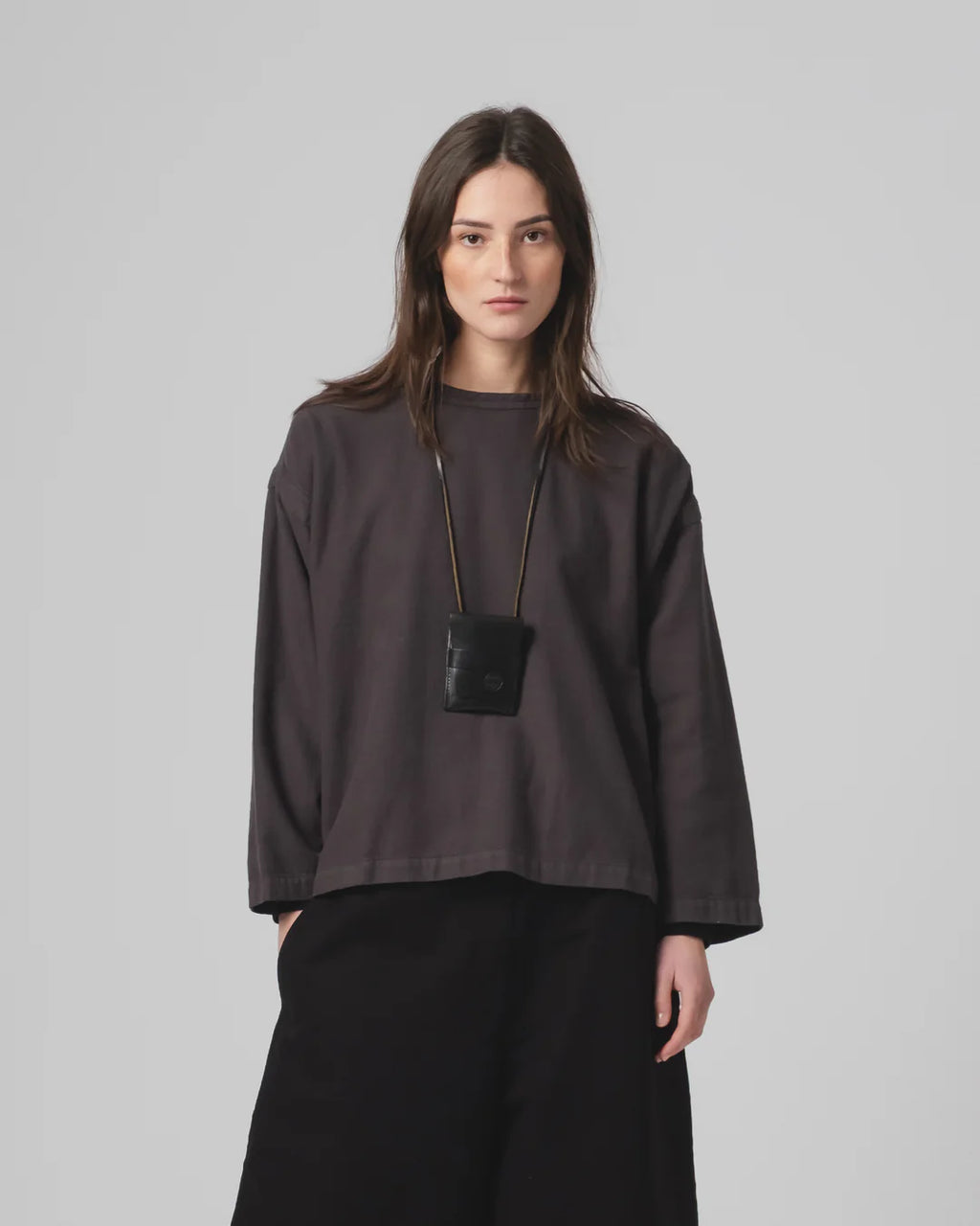 Woman wearing a Girls of Dust dark grey oversized shirt and black trousers against a plain background