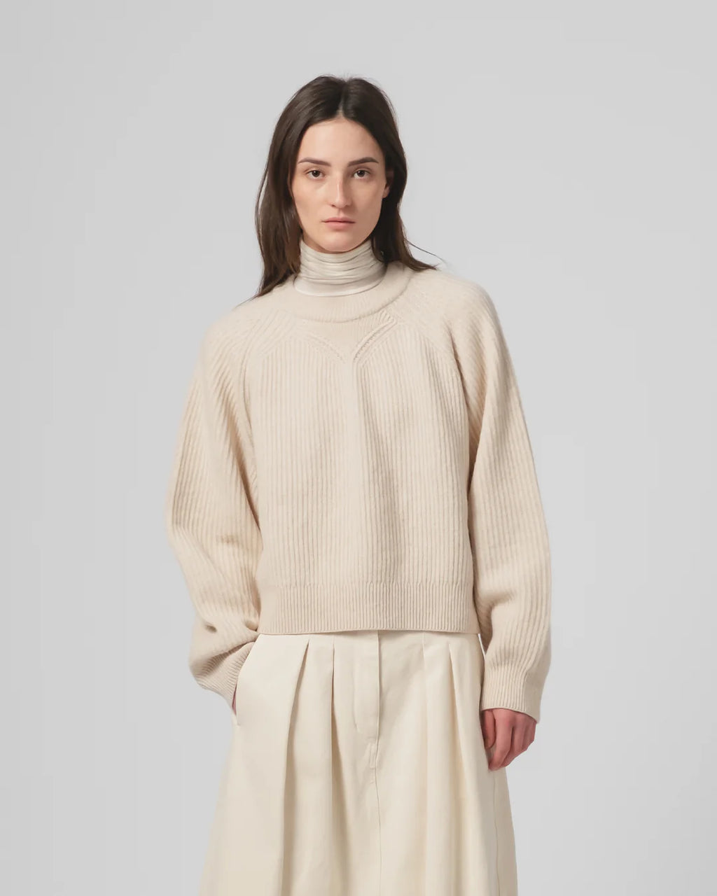 Woman wearing a Girls of Dust Ecru ribbed sweater and pants against a plain background