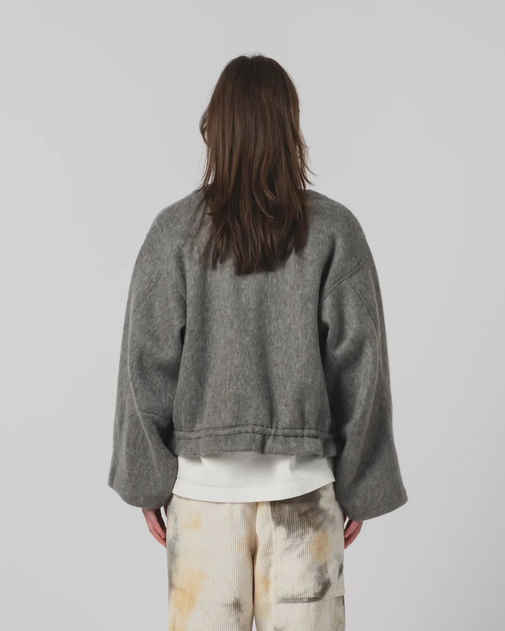 Person wearing a Girls of Dust grey jacket and light-coloured trousers against a plain background