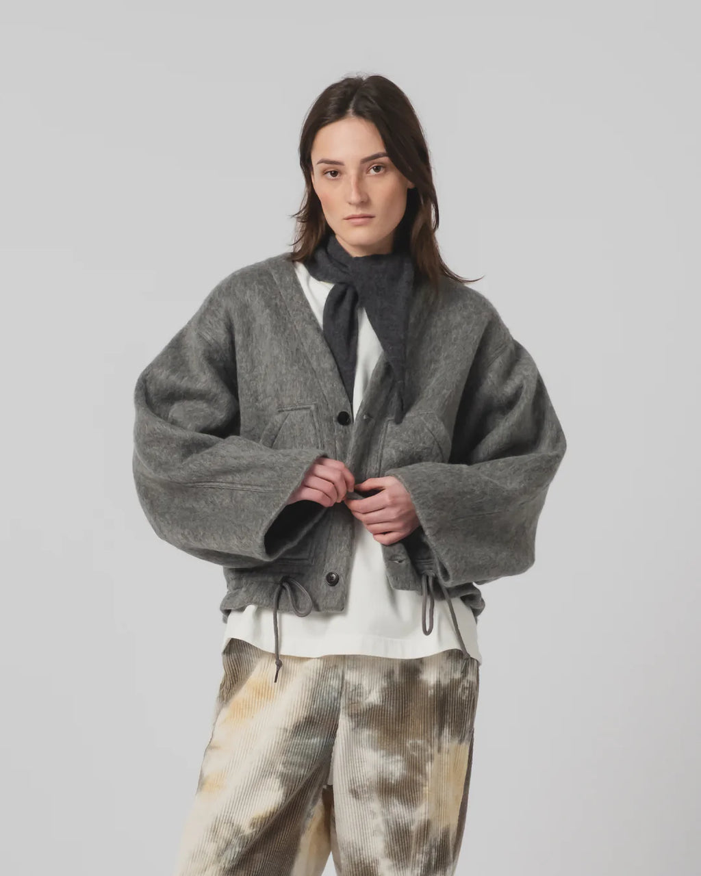 Person wearing a Girls of Dust grey oversized jacket over a white shirt with a neck scarf , standing against a plain background.