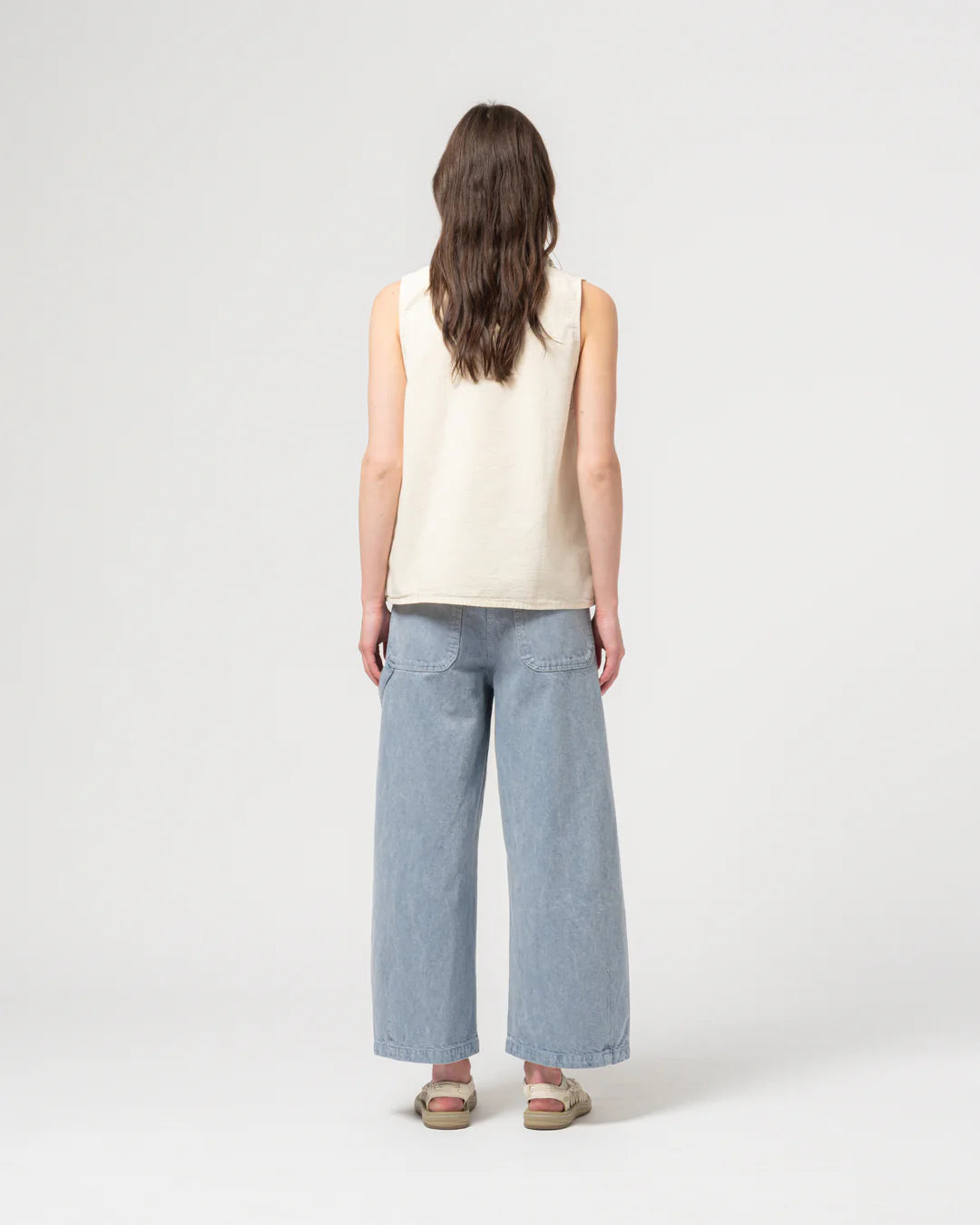 Person wearing a sleeveless cream top and light blue jeans on a white background