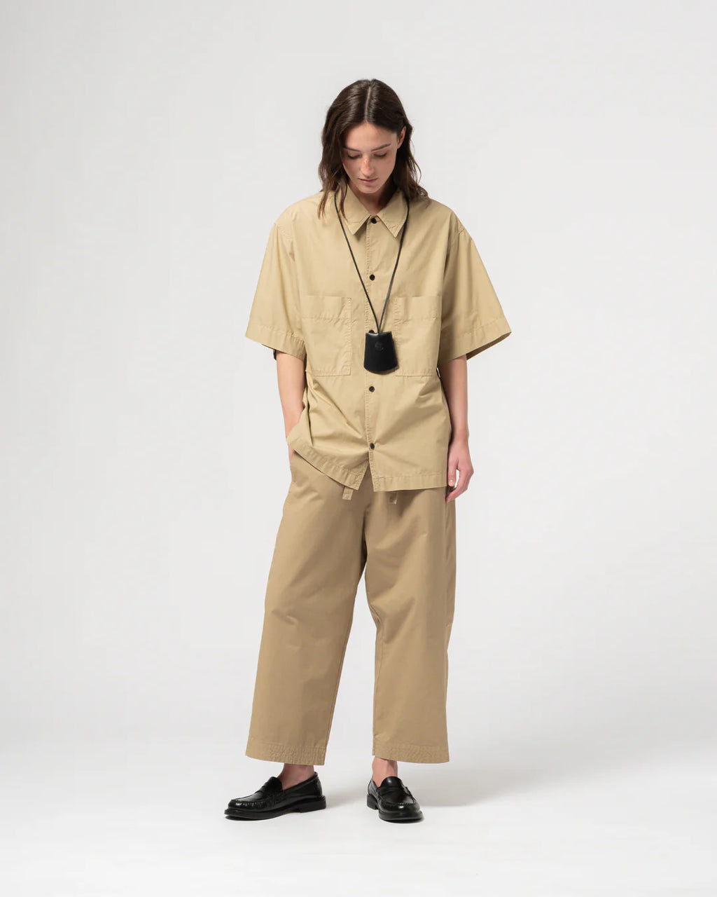 Person wearing Girls of Dust beige wide legged trousers with a matching shirt against a light grey background. 
