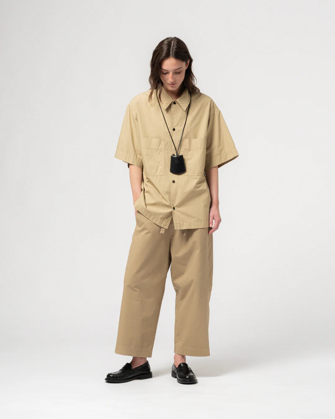 Person wearing Girls of Dust beige wide legged trousers with a matching shirt against a light grey background. 