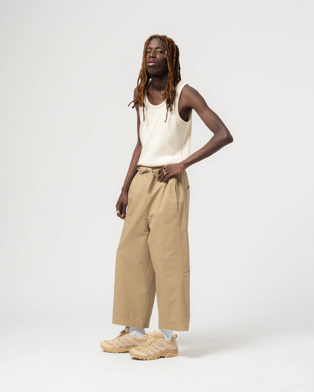 Person wearing a white tank top and beige pants on a white background