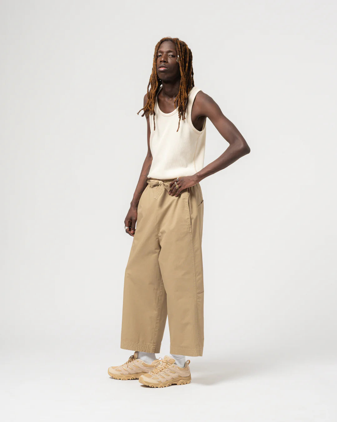 Person wearing a white tank top and beige pants on a white background