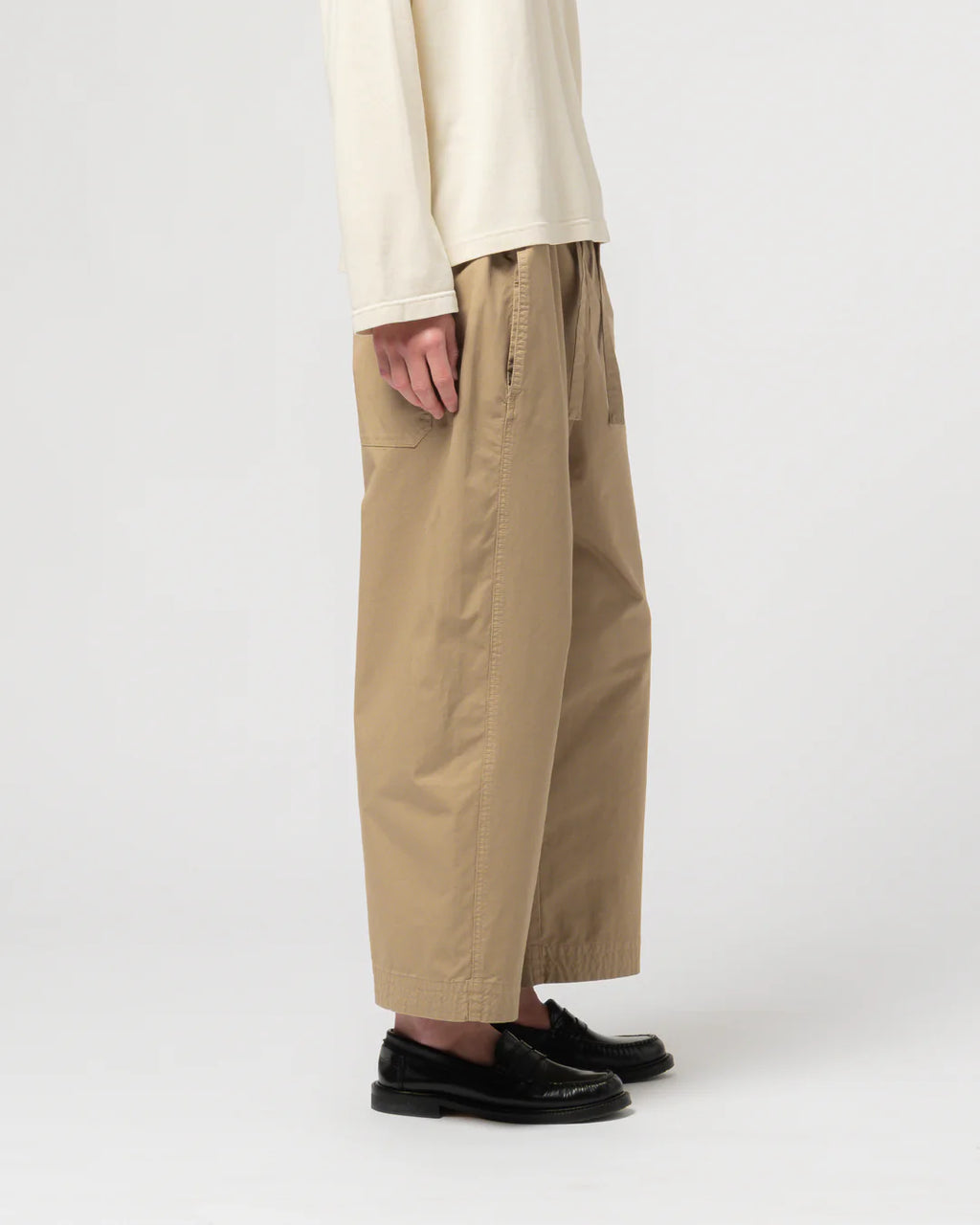Person wearing beige pants and a cream top on a white background