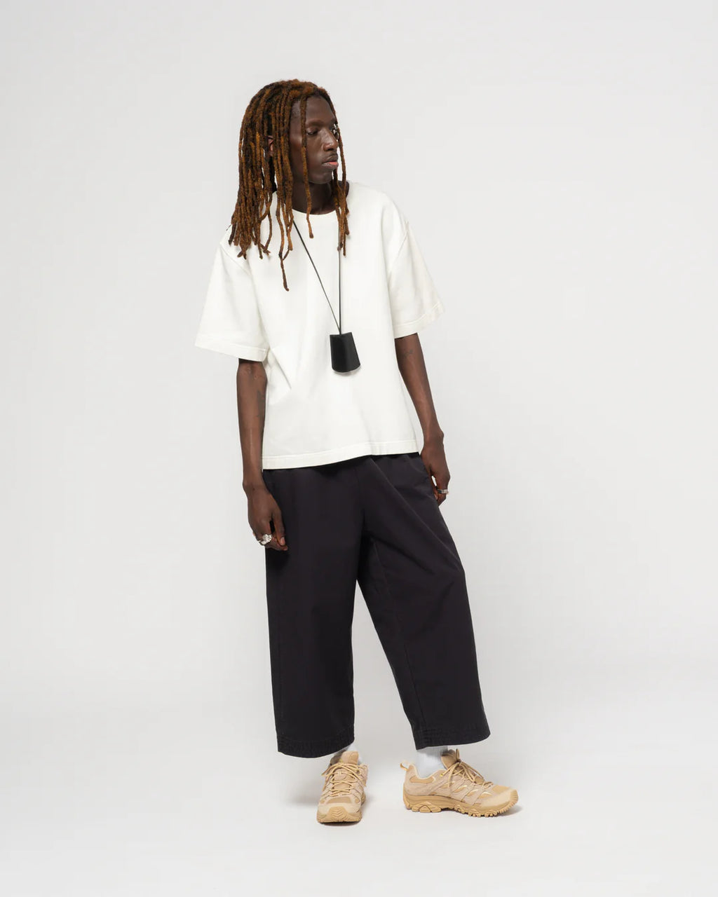 Person wearing a white t-shirt, black pants, and beige shoes on a white background