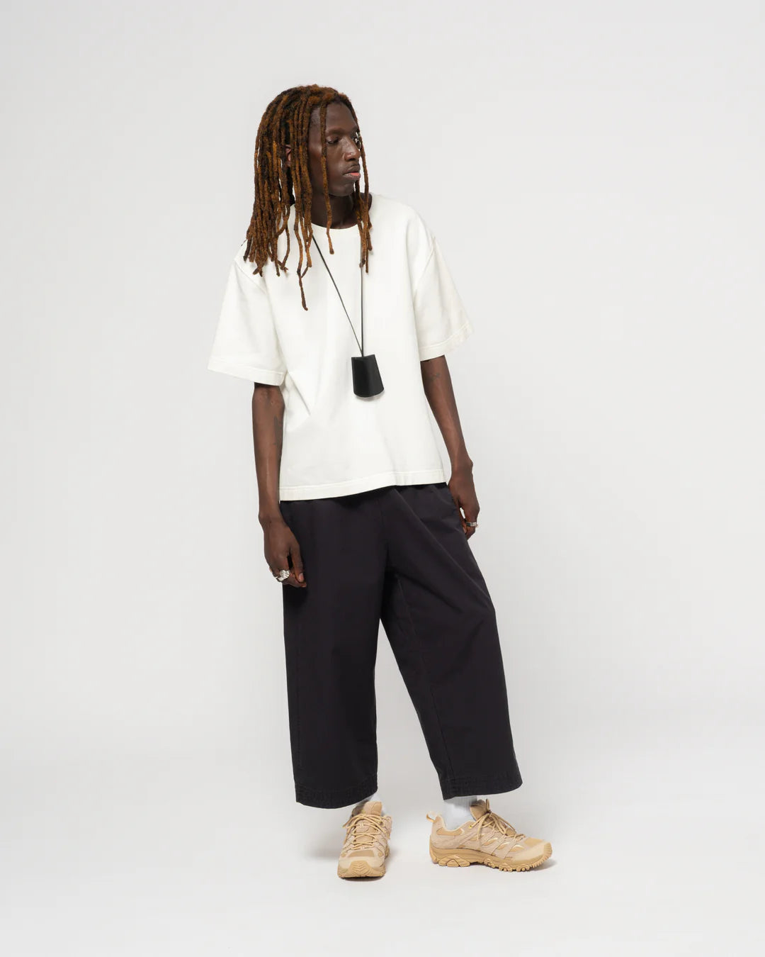 Person wearing a white t-shirt, black pants, and beige shoes on a white background
