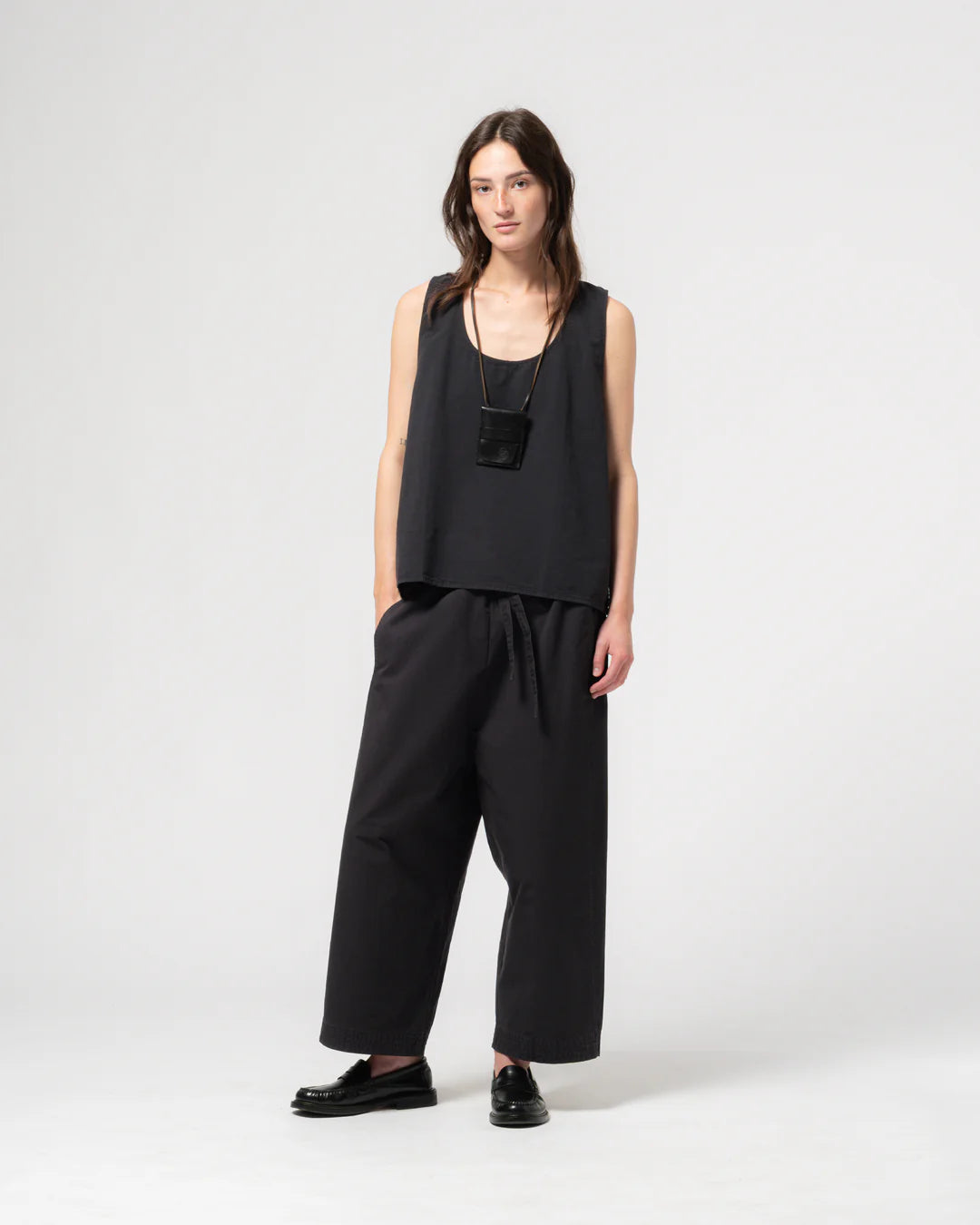 A person wearing Girls of Dust and Eat Dust Zen dark navy trousers with a matching vest top against a light grey background. 