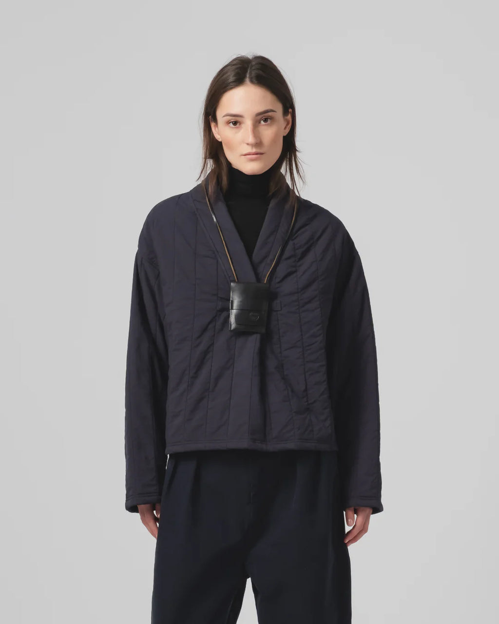 Person wearing a dark blue Girls of Dust sweater with a black bag over their shoulder on a light gray background