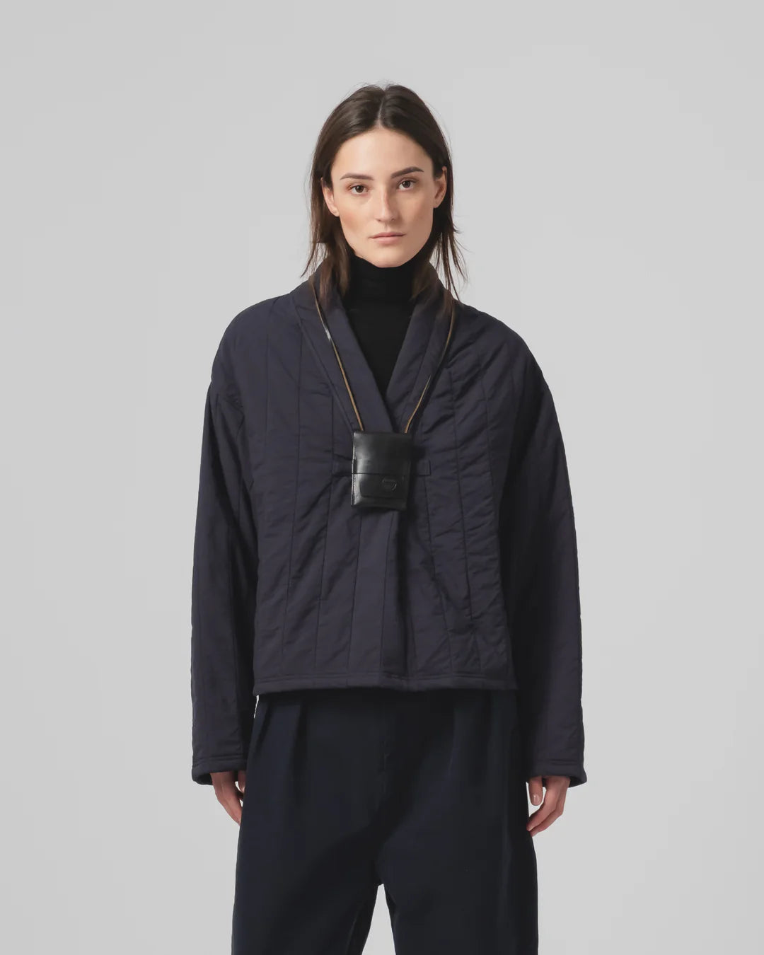 Person wearing a dark blue Girls of Dust sweater with a black bag over their shoulder on a light gray background