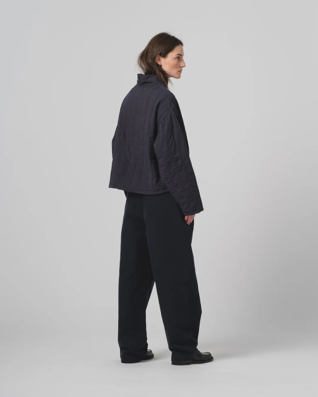 Person wearing a dark navy Girls of Dust sweater  and trousers on a light gray background