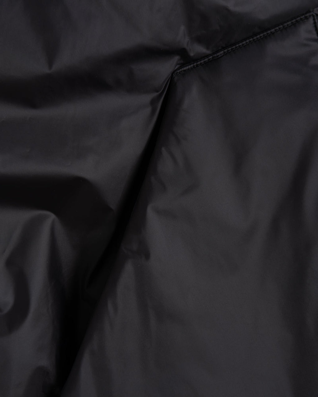 Close-up of a black fabric surface with visible folds and a seam, showing the material texture and color.