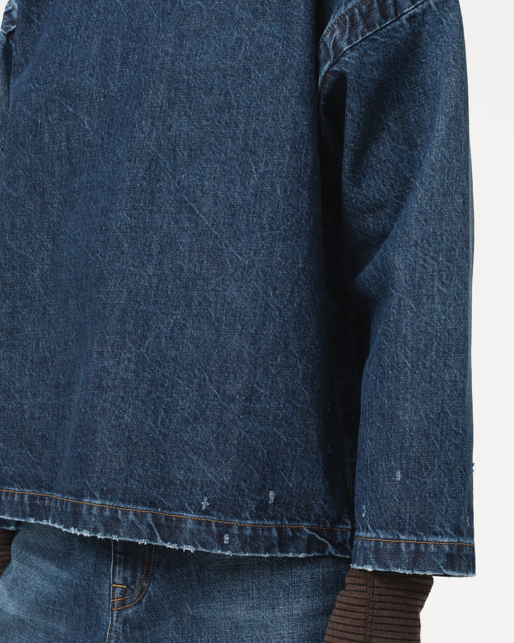 Close-up of a dark blue denim top with a raw, frayed hem and sleeve cuffs, paired with blue jeans and a brown ribbed top underneath.