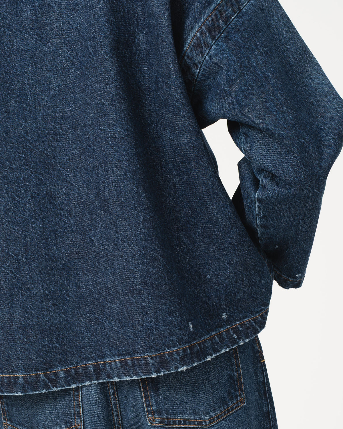 Close-up of a dark blue Girls of Dust Guard Smock Century Denim top with a frayed hem, paired with matching blue denim jeans against a light grey background.