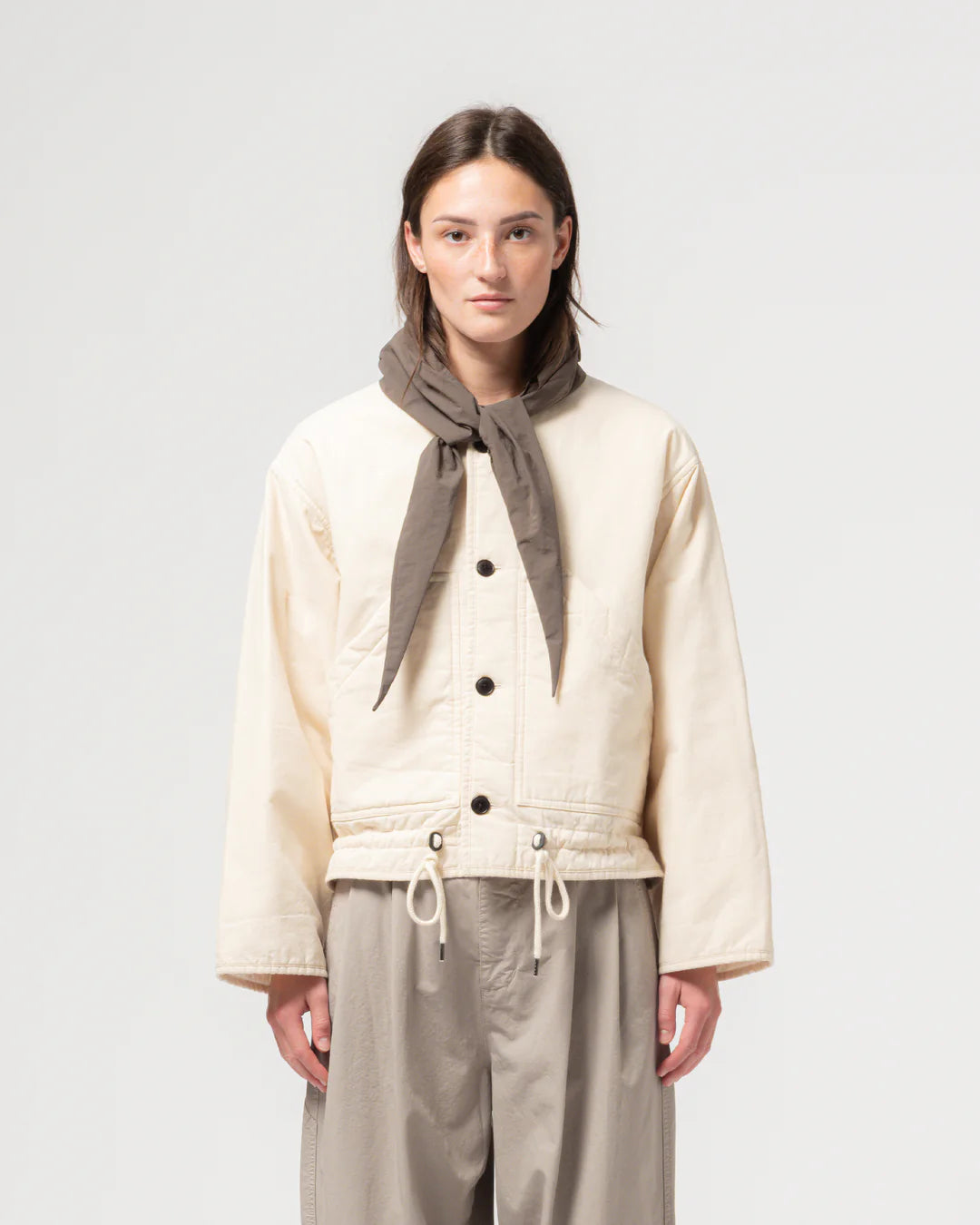 Person wearing a cream jacket with black buttons and beige pants, standing against a plain background.
