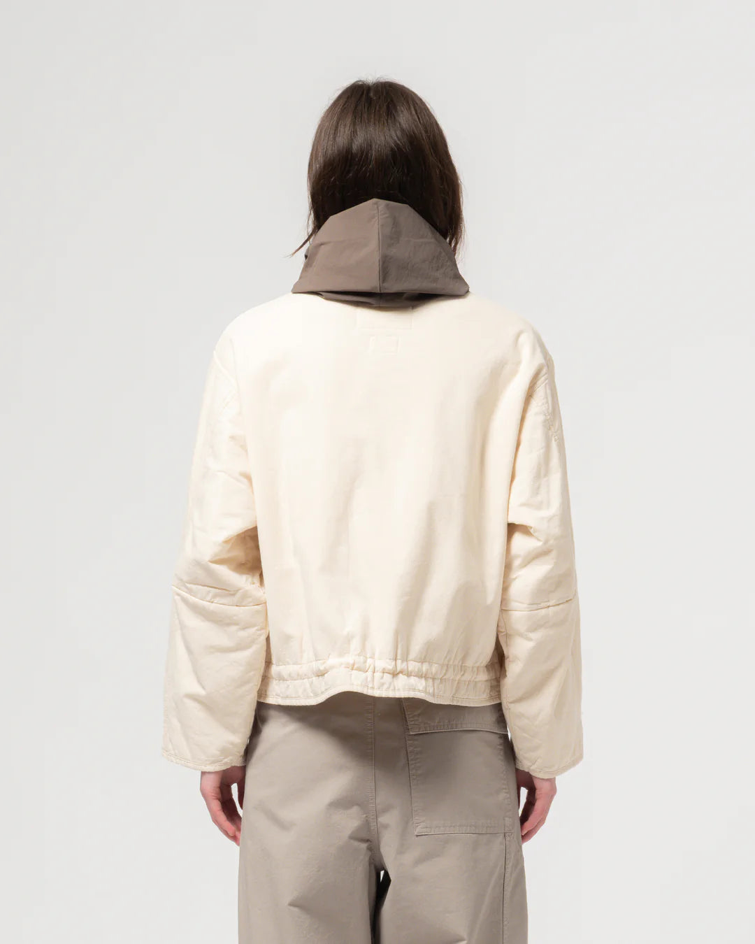Person wearing a beige jacket with a hood on a plain background