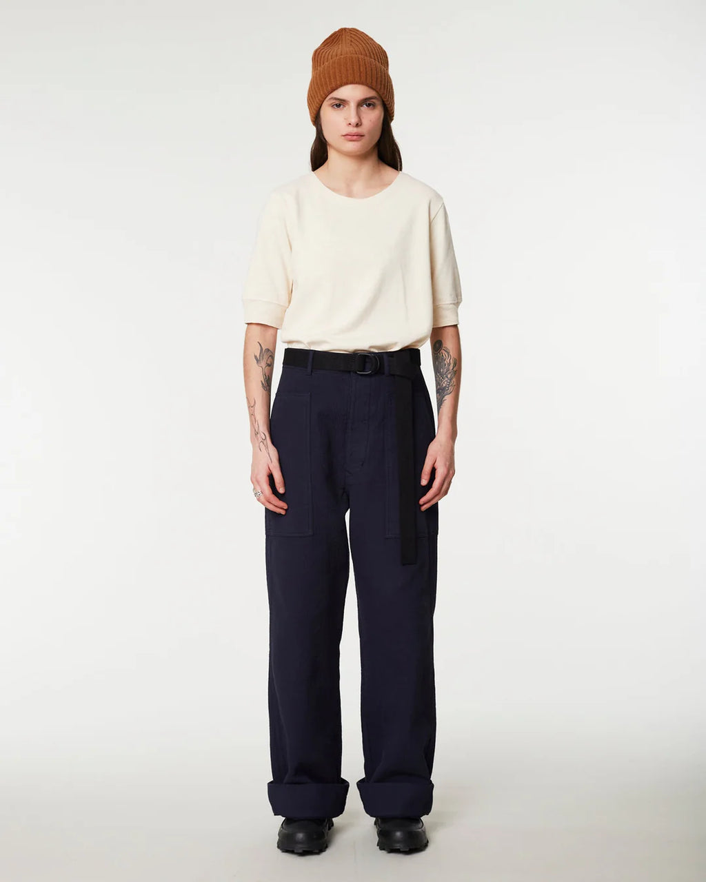 Person wearing a beige sweater, navy pants, and a brown beanie on a white background