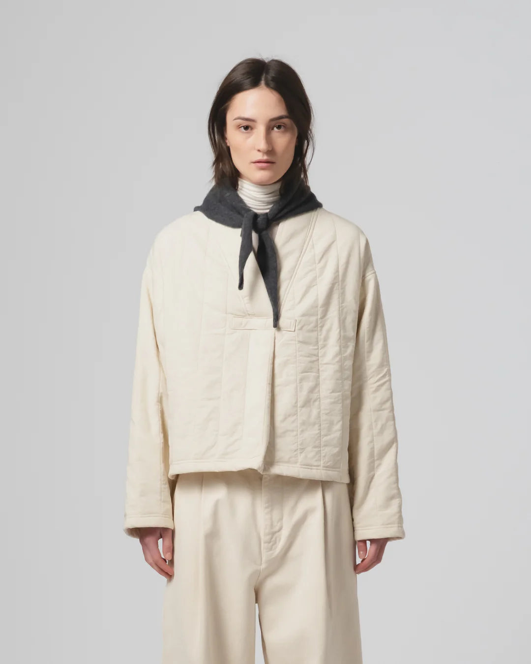 Person wearing a Girls of Dust ecru quilted jacket and pants with a grey scarf on a light grey background