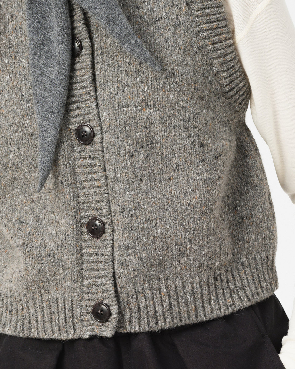 Close-up of Girls of Dust grey knit cardigan vest with dark buttons, worn over a white top 