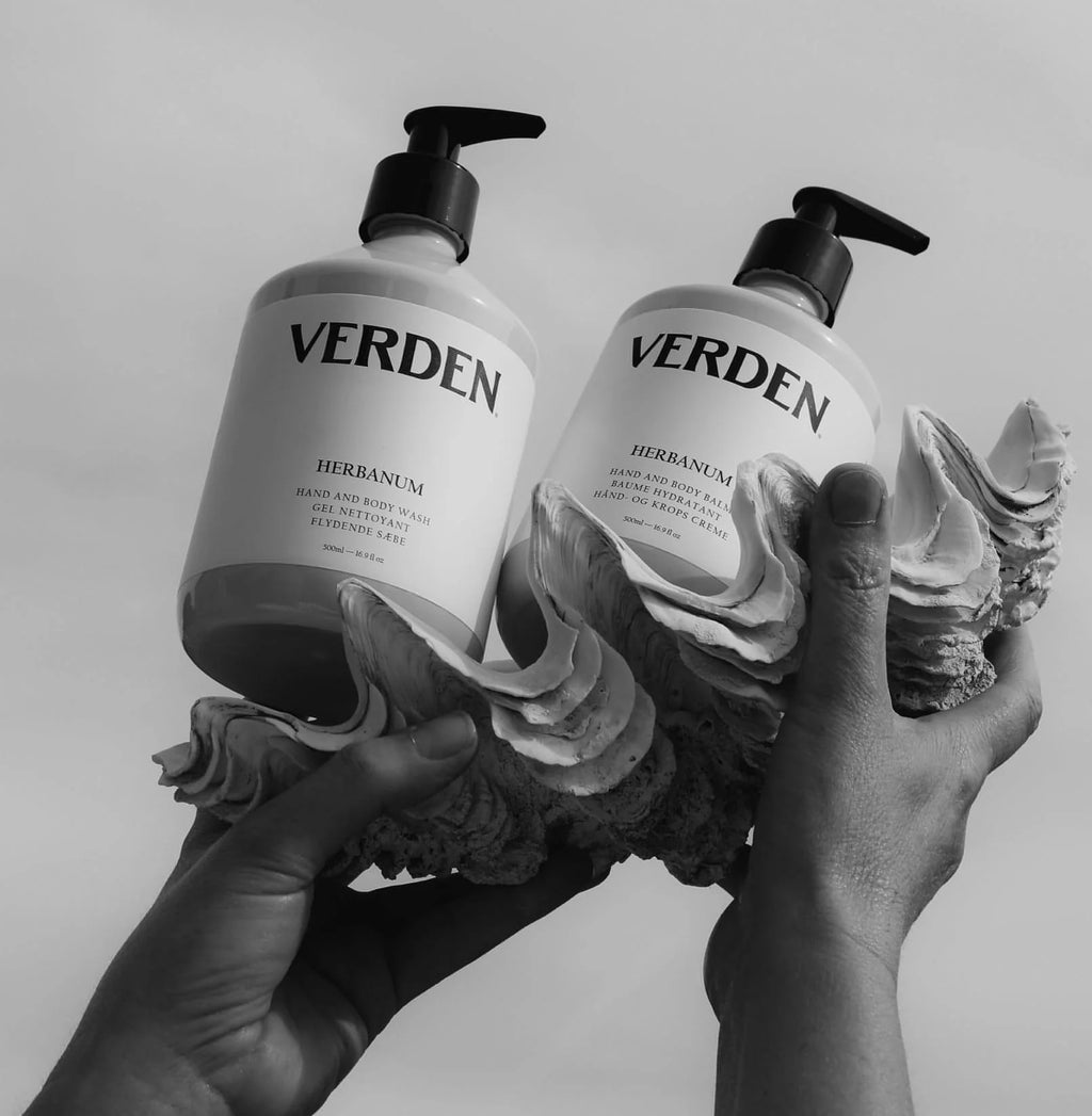 Two Verden body care products held by hands on a shell against a light background